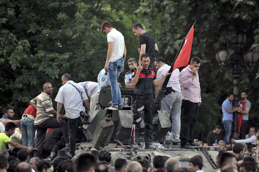 A Turkish policeman and other people stand atop of a military vehicle in Ankara